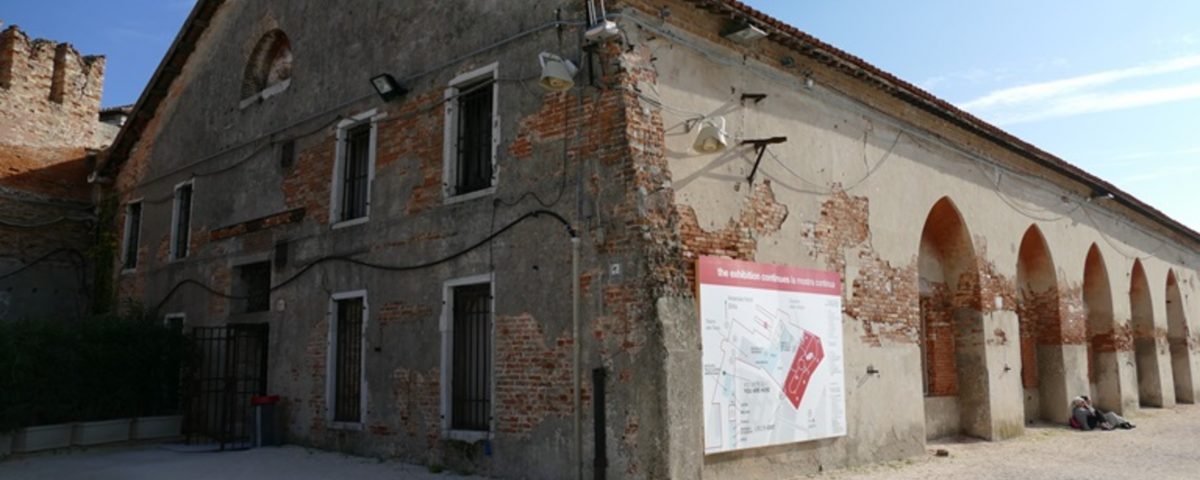 Outside view of Tesa dell'Isolotto. An old, long brick building, with craved archways cut into the right side of the building.