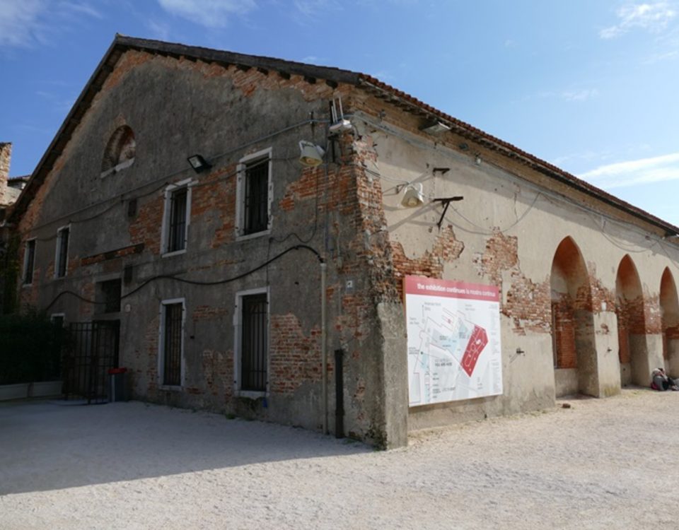 Outside view of Tesa dell'Isolotto. An old, long brick building, with craved archways cut into the right side of the building.