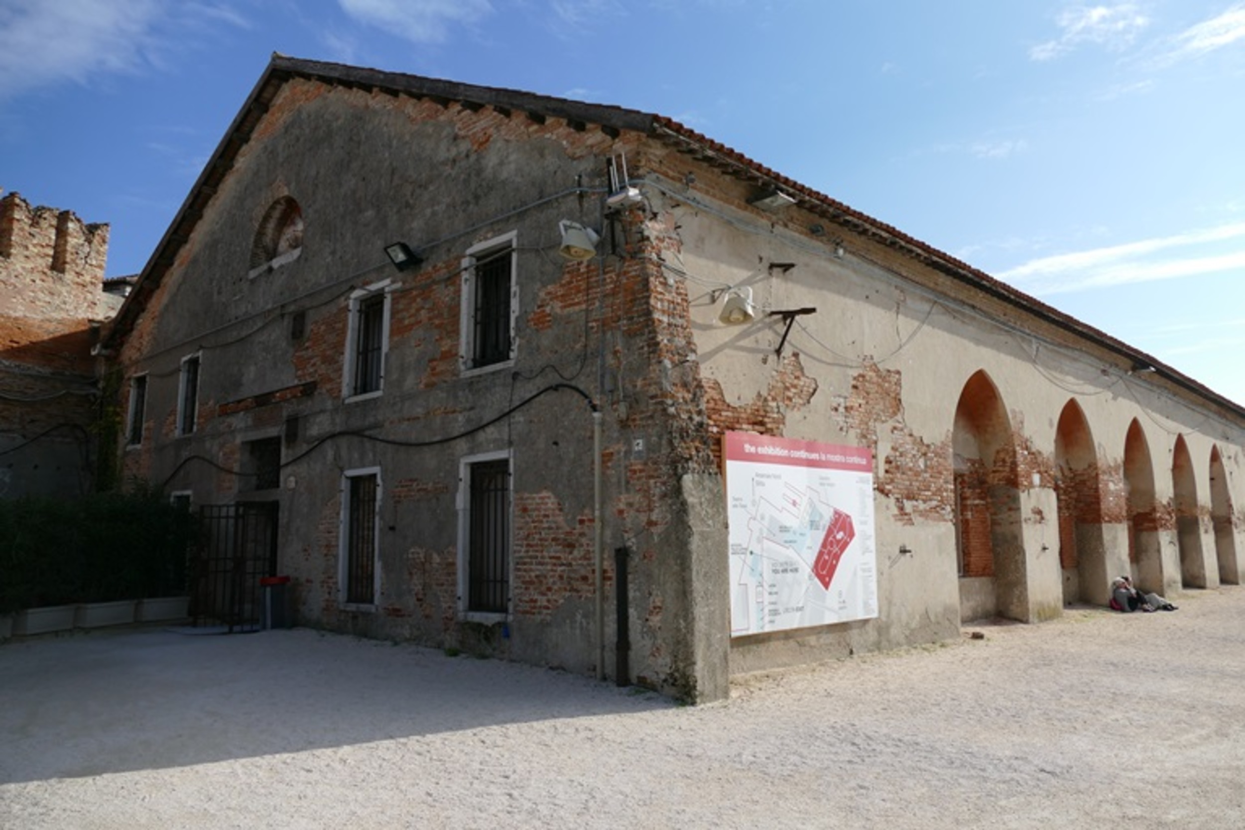 Outside view of Tesa dell'Isolotto. An old, long brick building, with craved archways cut into the right side of the building.