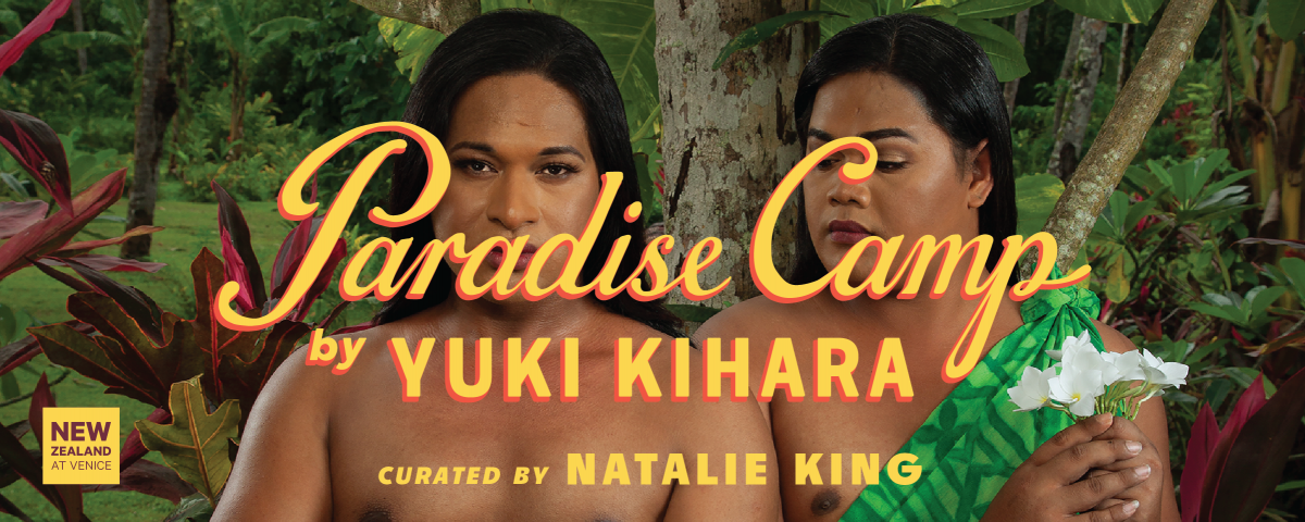 A photograph of two people standing in front of trees and plants. The person on the left is holding a plate of food. There is yellow text across the image reading Paradise Camp by Yuki Kihara, curated by Natalie King. There is a logo in the bottom left corner that is a yellow square reading New Zealand at Venice.