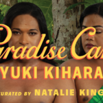 A photograph of two people standing in front of trees and plants. The person on the left is holding a plate of food. There is yellow text across the image reading Paradise Camp by Yuki Kihara, curated by Natalie King. There is a logo in the bottom left corner that is a yellow square reading New Zealand at Venice.