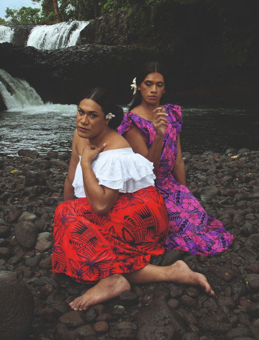 Two Fa‘afafine (Samoa’s third gender) in bright clothing on a rocky riverbed. Front figure looks directly at the camera.