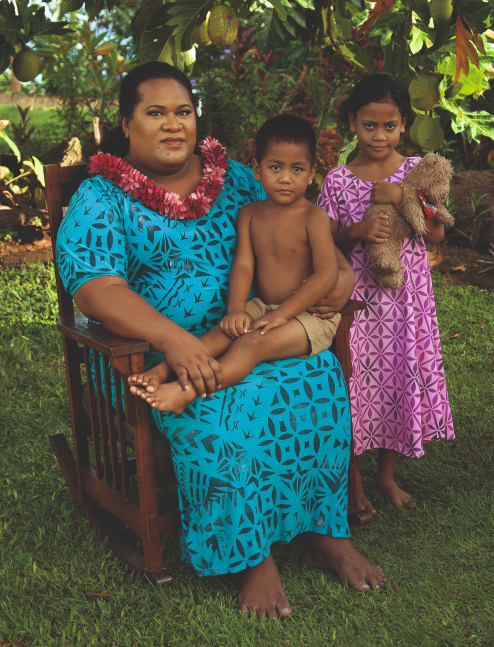 ●	Fa‘afafine (Samoa’s third gender) on a rocking chair with a young boy on their lap, a young girl stands with a teddy bear. 